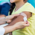 Closeup of doctor putting a band-aid over a vaccine site on a young person's arm