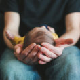 Closeup of person's hands holding a baby in their lap