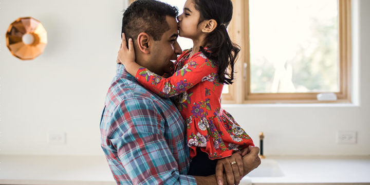 Father holding daughter in arms while she kisses his forehead