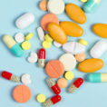 Variety of different sized and different colored pills sitting on blue background
