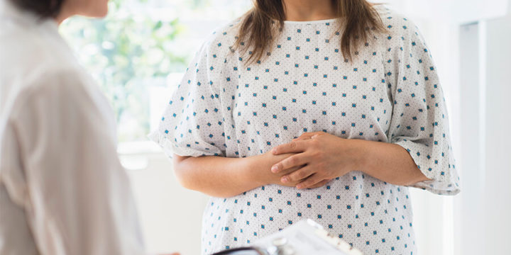 Woman with hands over stomach talking to doctor in a doctor's office