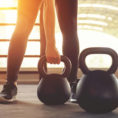 Closeup of someone lifting a kettlebell surrounded by other kettlebells of various sizes in a gym