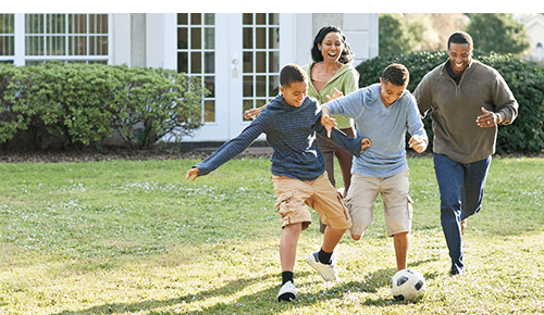 Parent and two children playing soccer in their backyard