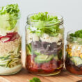 Different sizes of glass mason jars with different types of salad in them