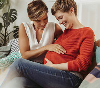 Pregnant person next to partner who has their hand on their stomach