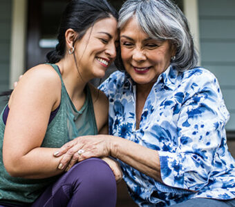 Older woman hugging adult daughter on house porch