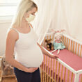 Pregnant woman wearing face mask standing next to baby crib