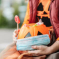 Child holding pumpkin candy basket that has a face mask sitting over it