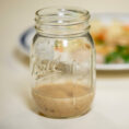 Mason jar filled with peanut sauce sitting in front of a plate full of chicken and vegetables