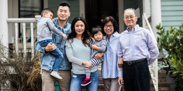 Three generations of an Asian family smiling and standing in front of house