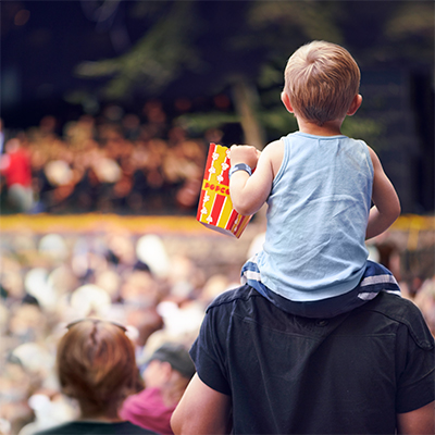 Child on father's shoulders listening to music at festival