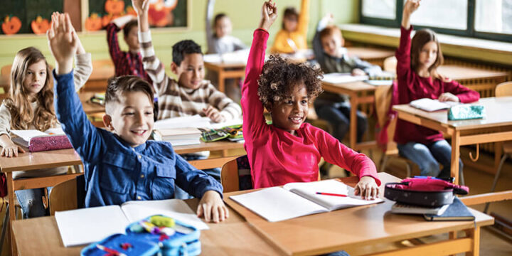 School children in class with their hands raised