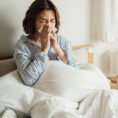 Sick person blowing their nose while sitting in bed