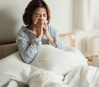 Sick person blowing their nose while sitting in bed