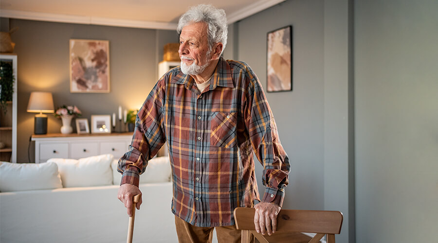 Senior man holding a cane holding onto a chair for balance in home