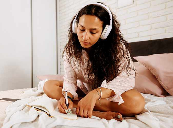 woman sitting in bed listening to music and journaling
