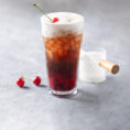 Creamy soda in glass with cherries next to it