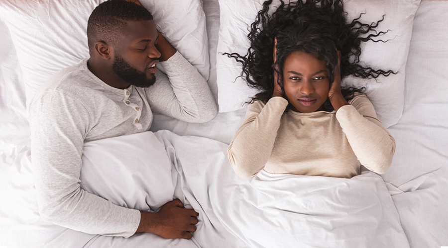 man snoring woman holding ears in bed