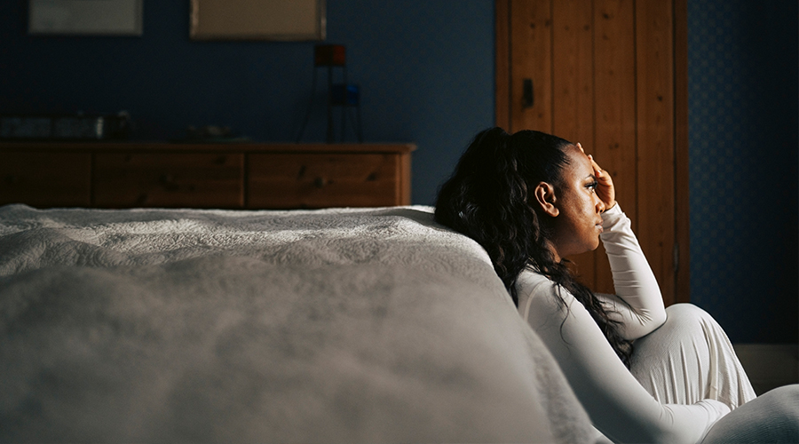 Woman sitting at edge of her bed upset